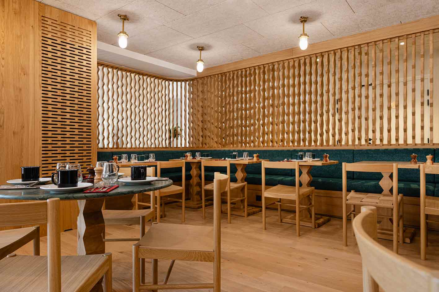 Espace restaurant & PDJ de l'hôtel la Couronne à Chamonix74. Le mobilier est en bois et le piétement de table a des motifs géométriques que l'on retrouve sur la cloison bois ajourée pour une ambiance chaleureuse. Vue générale de la salle