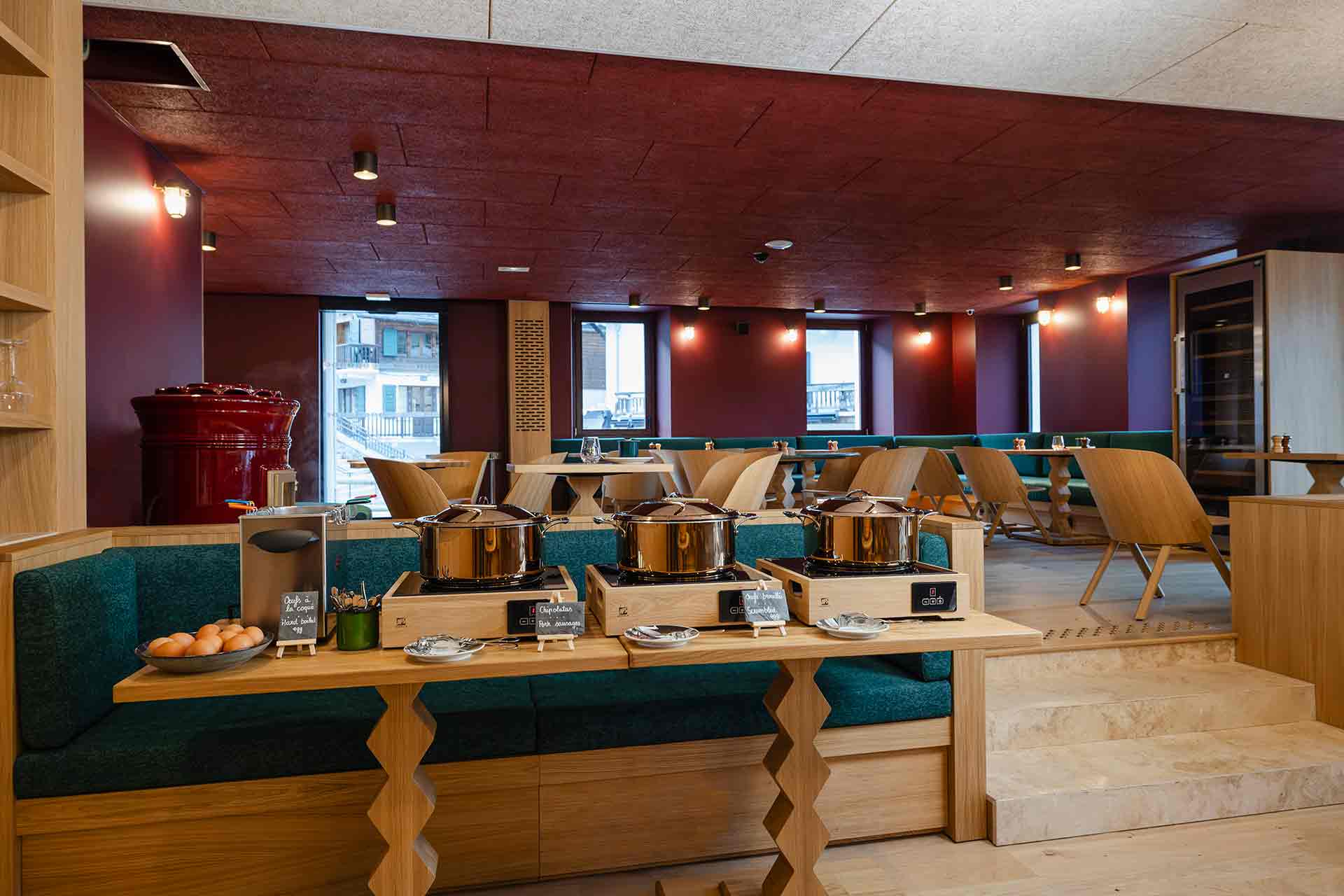 Espace petit déjeuner de l'hôtel la Couronne à Chamonix74 avec du mobilier en bois clair, des banquettes vertes et des peintures rouges.