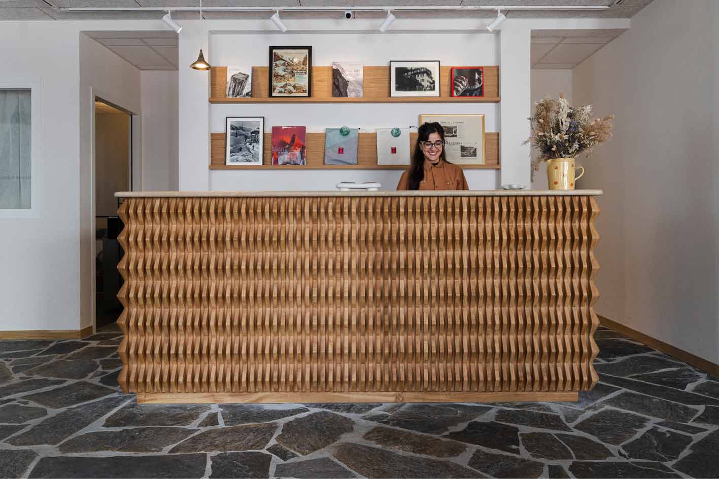 Comptoir d'accueil en bois sculpté avec un motif géométrique, conçu sur mesure pour l'hôtel Couronne à Chamonix, mettant en avant un design artisanal et chaleureux dans un espace contemporain