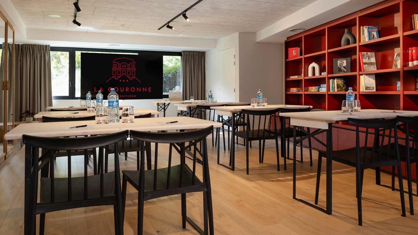 Salle polyvalente de l'hôtel la Couronne présentée en salle de formation à Chamonix74 avec un sol en parquet clair, des murs blancs et une immense bibliothèque rouge