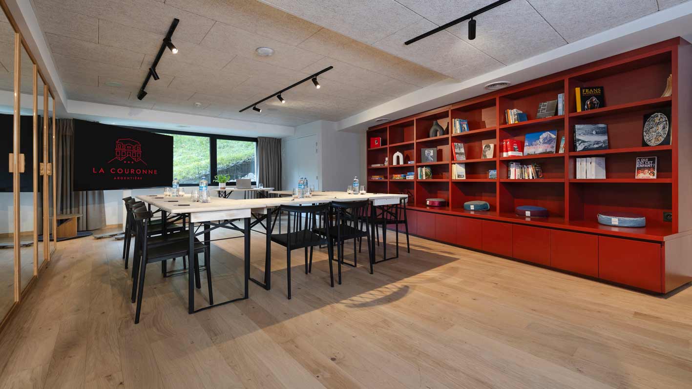 Salle polyvalente de l'hôtel la Couronne présentée en salle de conférence à Chamonix74 avec un sol en parquet clair, des murs blancs et une immense bibliothèque rouge