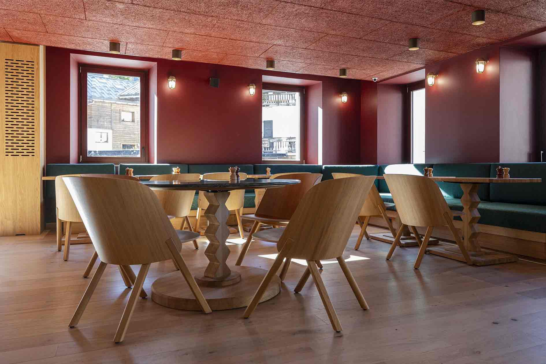 Restaurant de l'hôtel la Couronne à Chamonix74. les chaises et les tables sont en bois. Les tables ont un piétement géométriques dans un style de montagne. Pour compléter le côté chaleureux, les murs et le plafond sont rouges